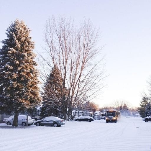 Snow-covered neighborhood street with parked cars and snowplow clearing winter road